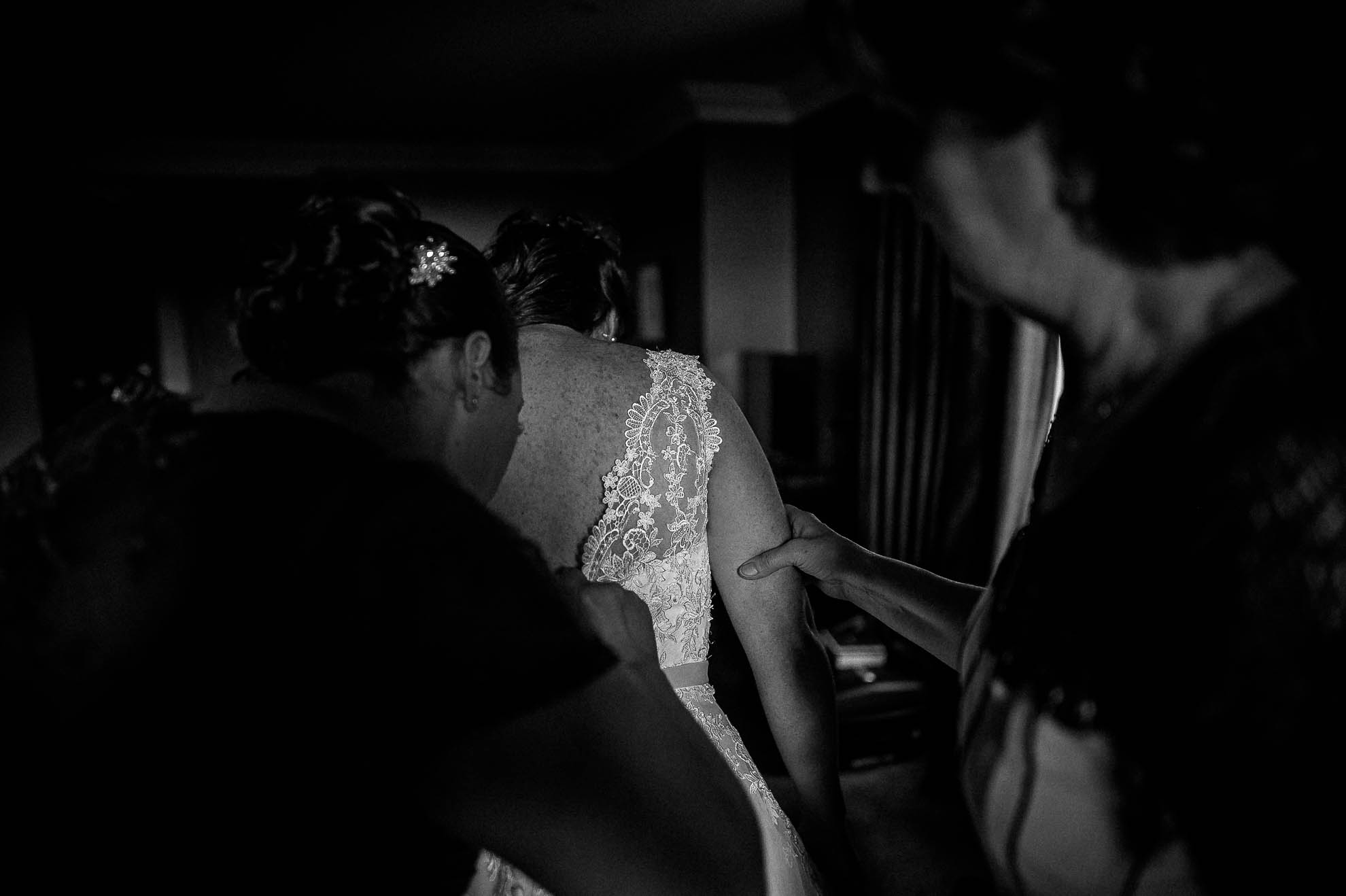 Bridesmaids help bride into dress