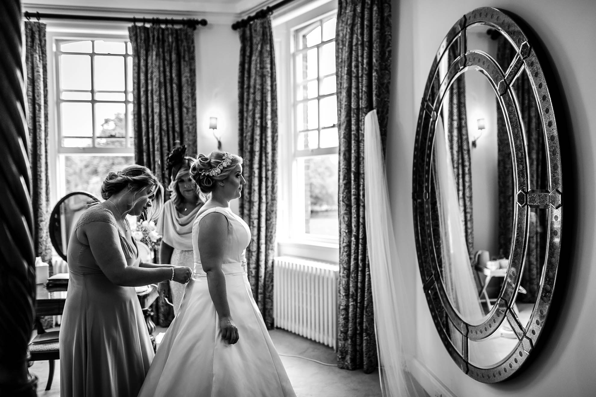 Bride looking in mirror as bridesmaid adjusts her dress