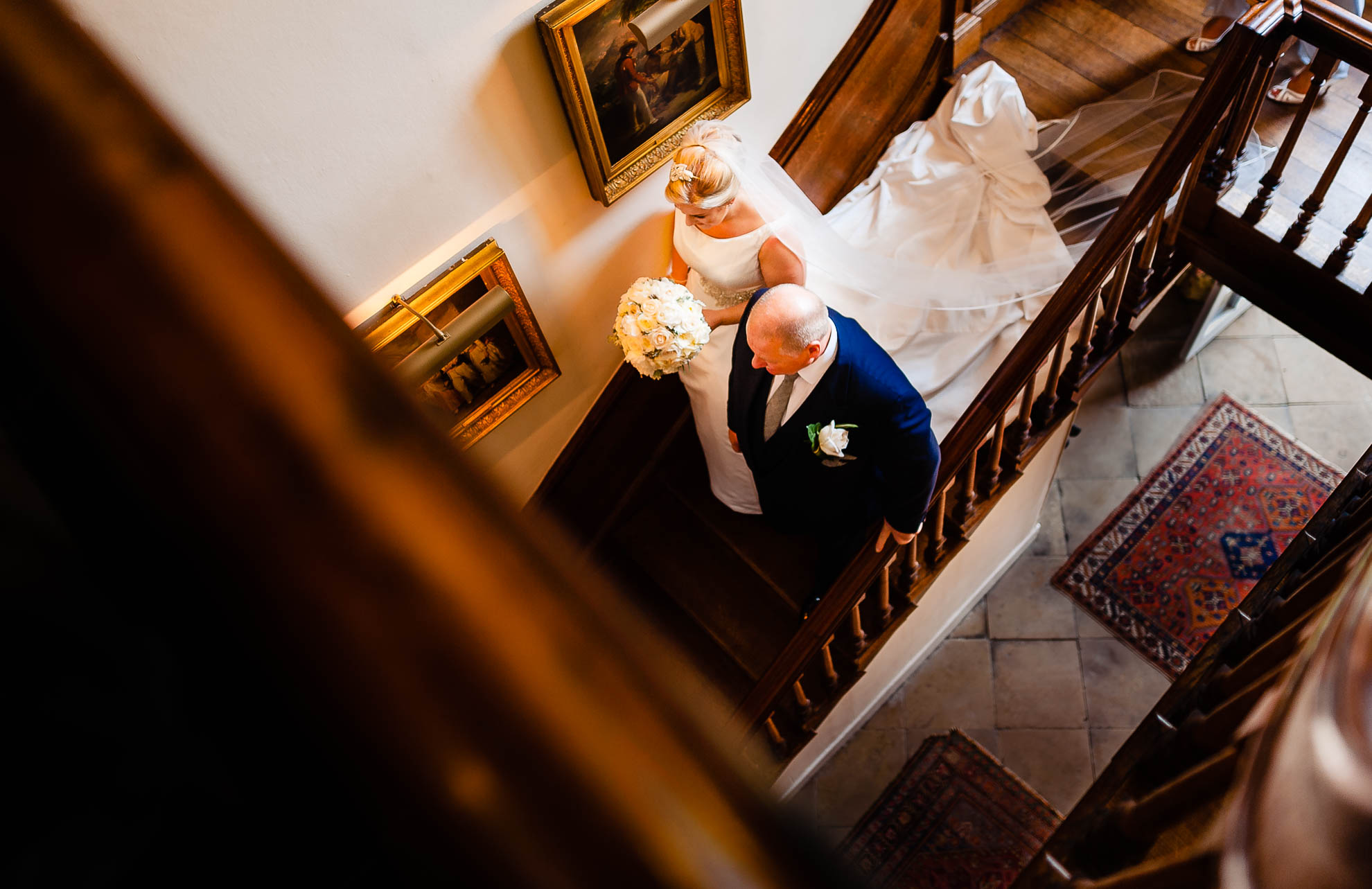 Bride walks down stairs with father towards wedding ceremony