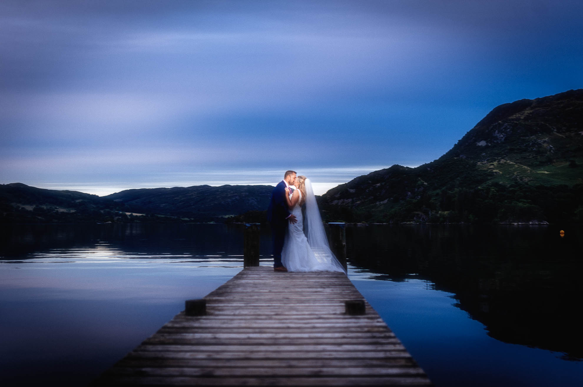 Bride and groom stand at end of jetty kissing