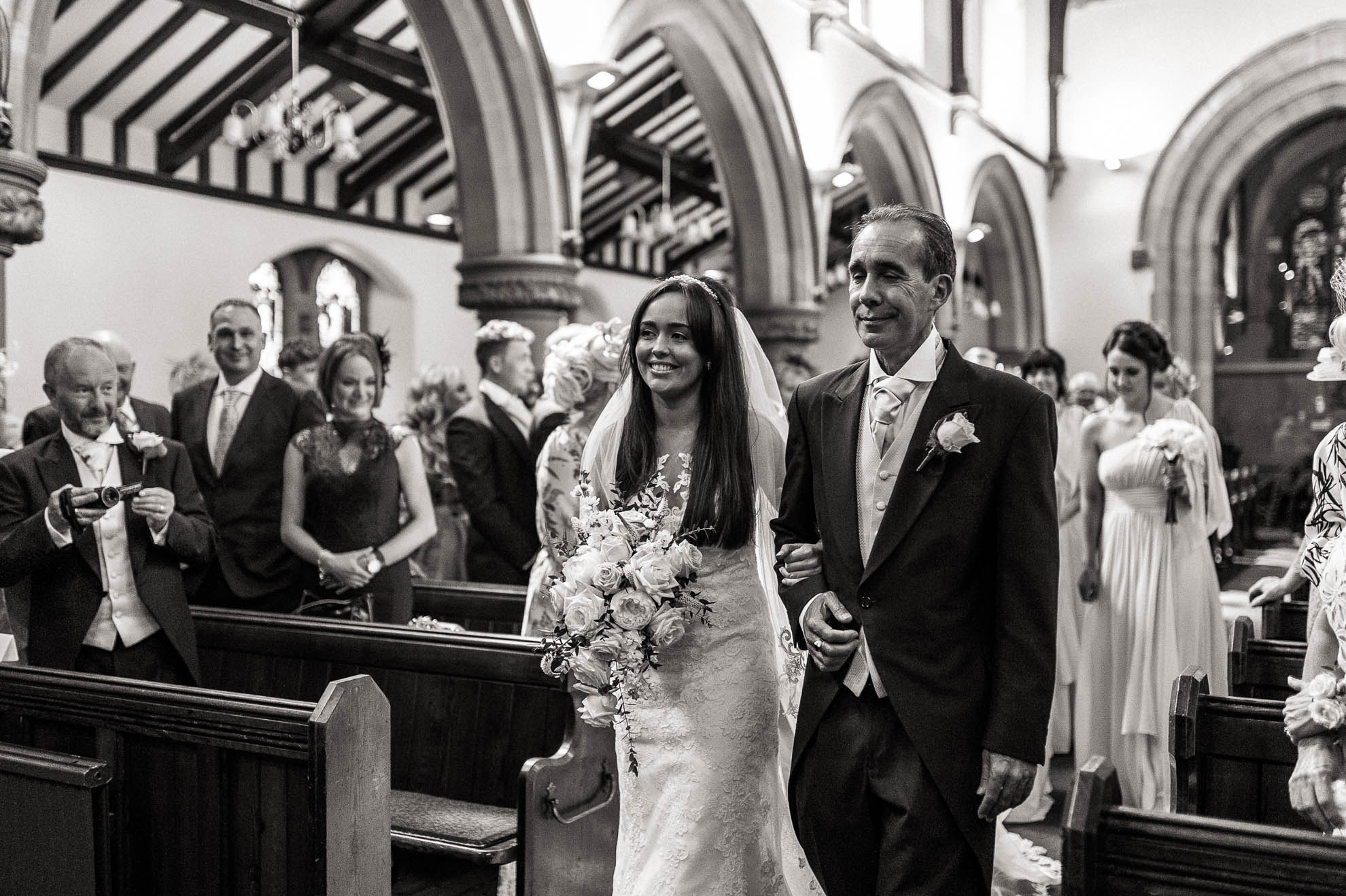 the bride smiles at the groom as she walks up the church aisle with her father