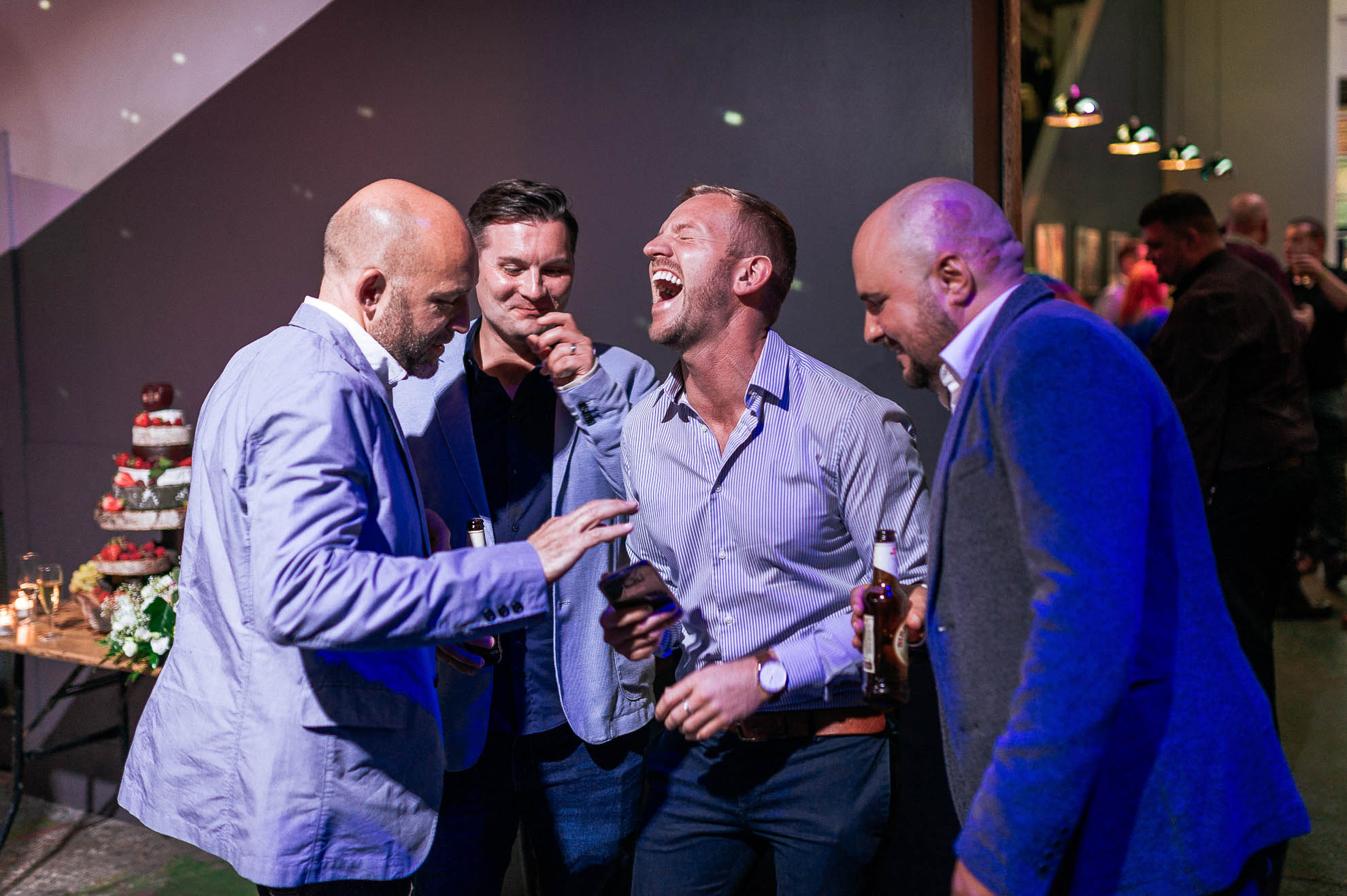 wedding guests laugh at an image on a phone.