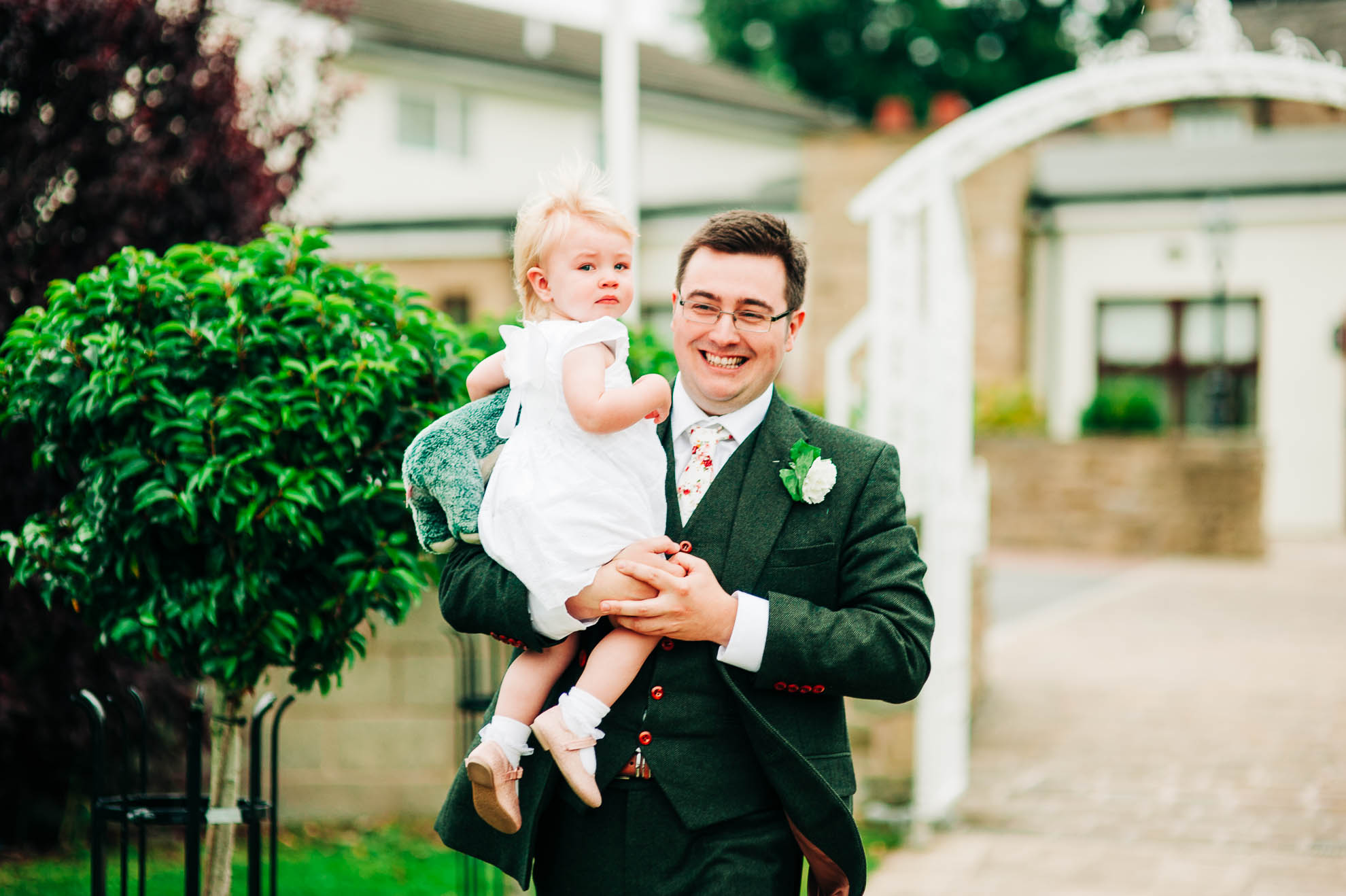 Groom holds flower girl as he walks to the pavillion