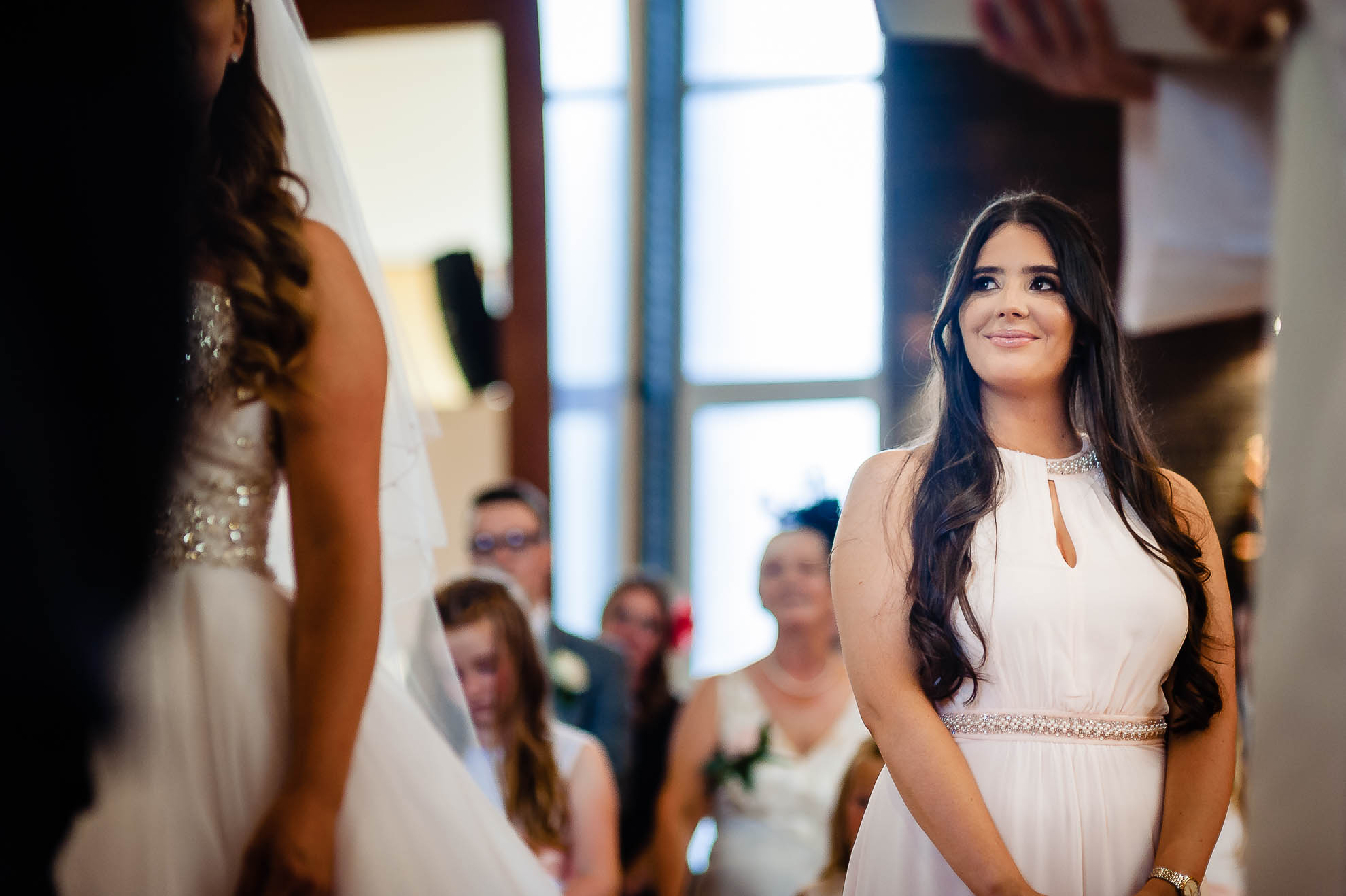 Bridesmaid smiling as she watches the bride and groom during the ceremony