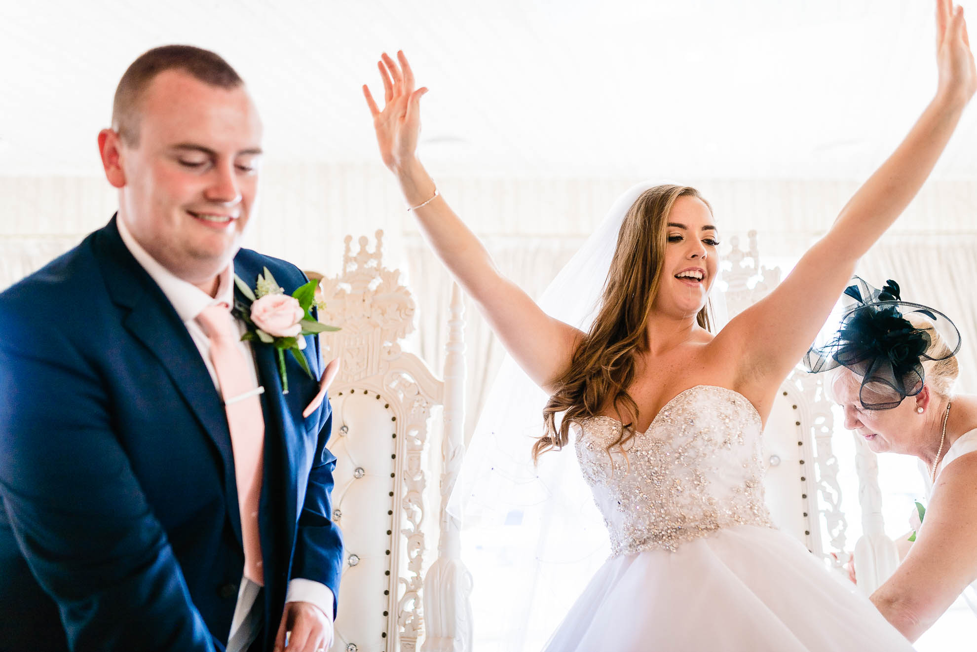 bride wih hands up in the air as she sits at the top table