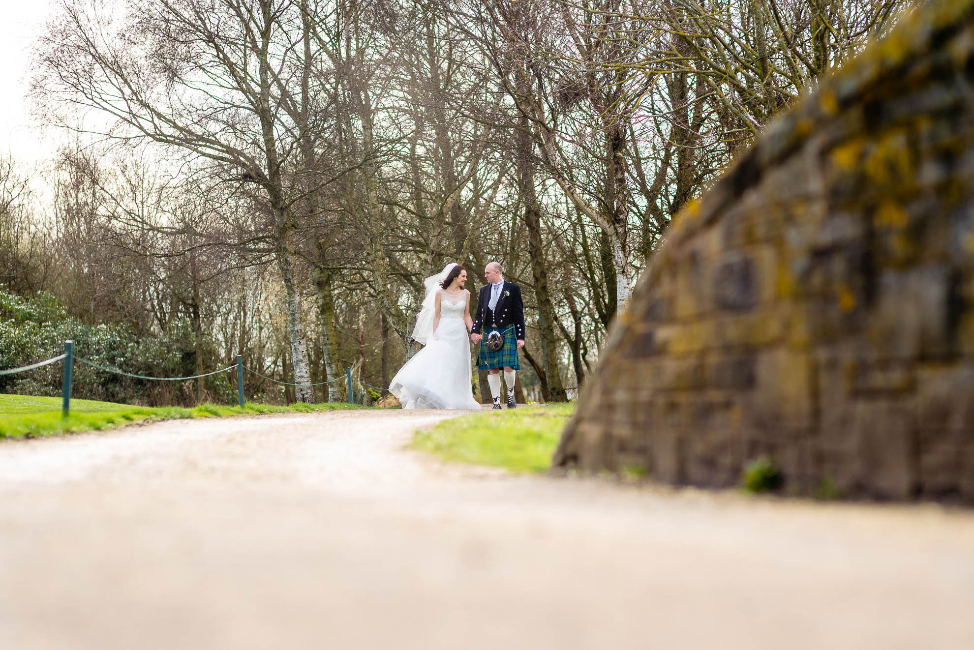Bride and groom walk towards a bridge hand in hand