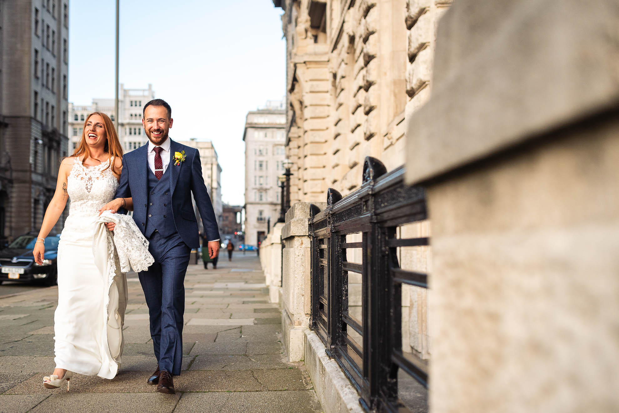 Bride and groom share a joke as they walk around the Three Graces in liverpool