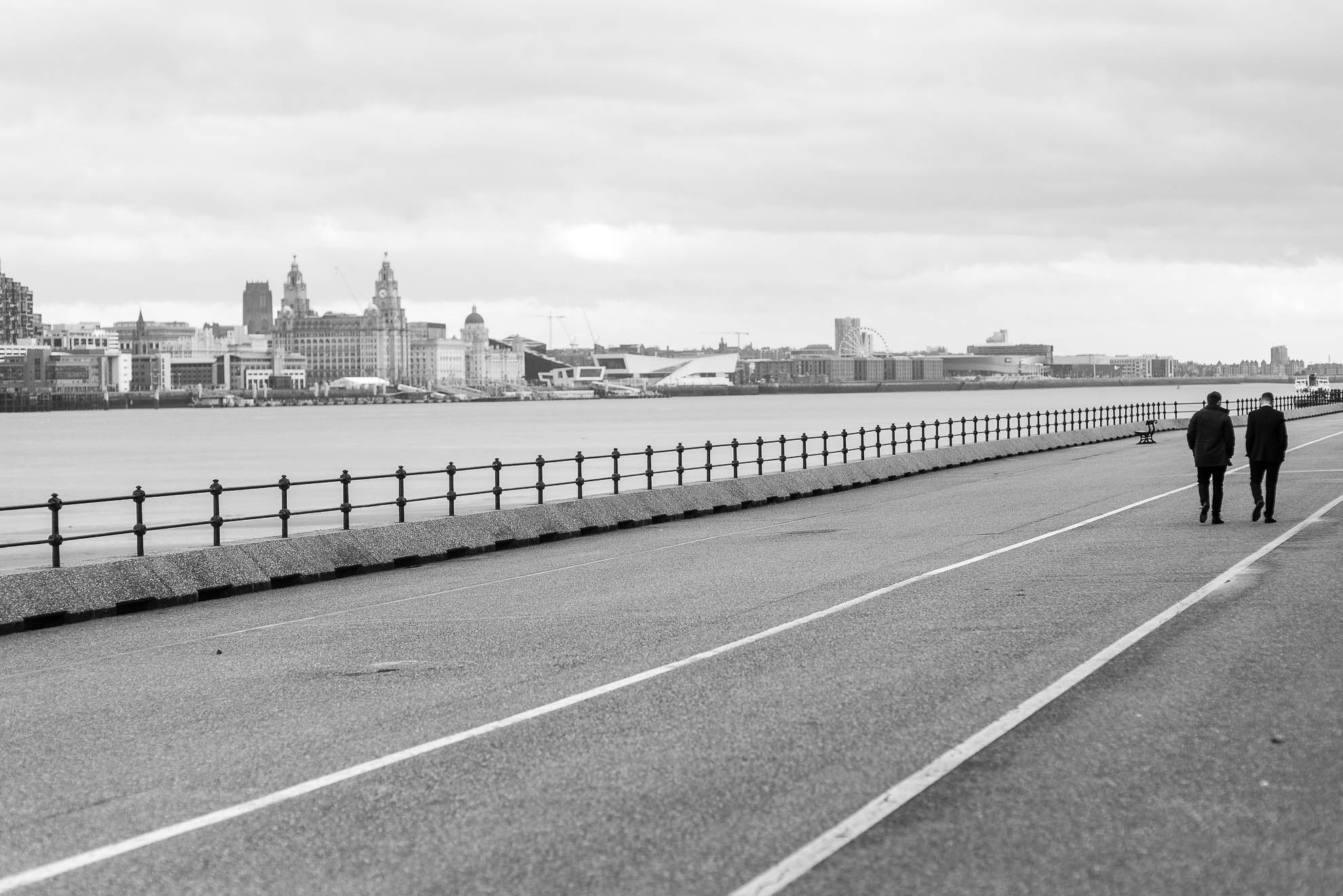 Groom and best man walk down Mersey waterfront
