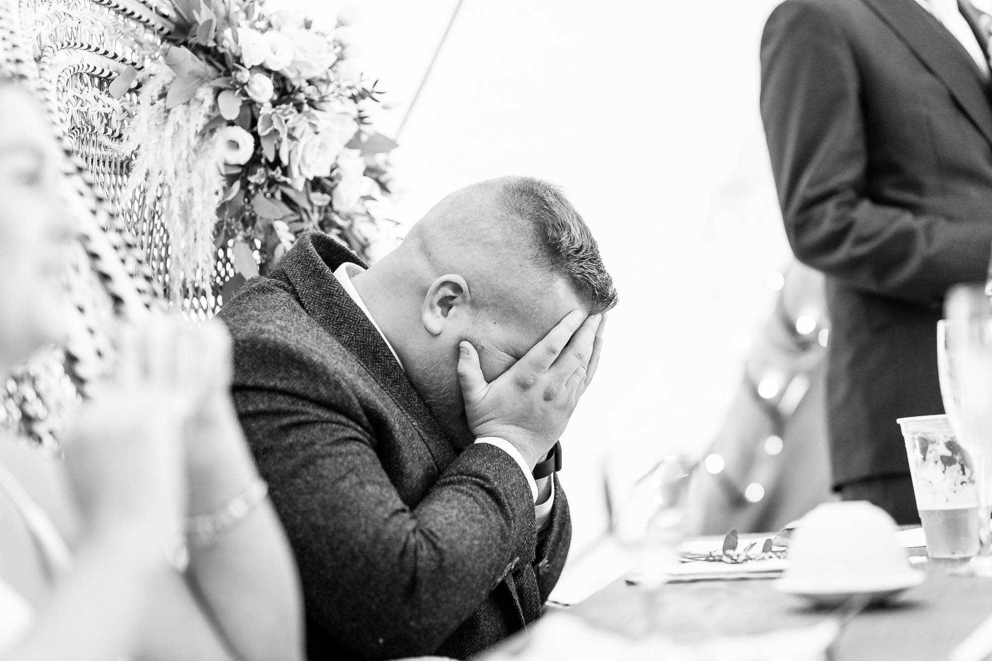 Groom holds face in hands in embaressment during speeches
