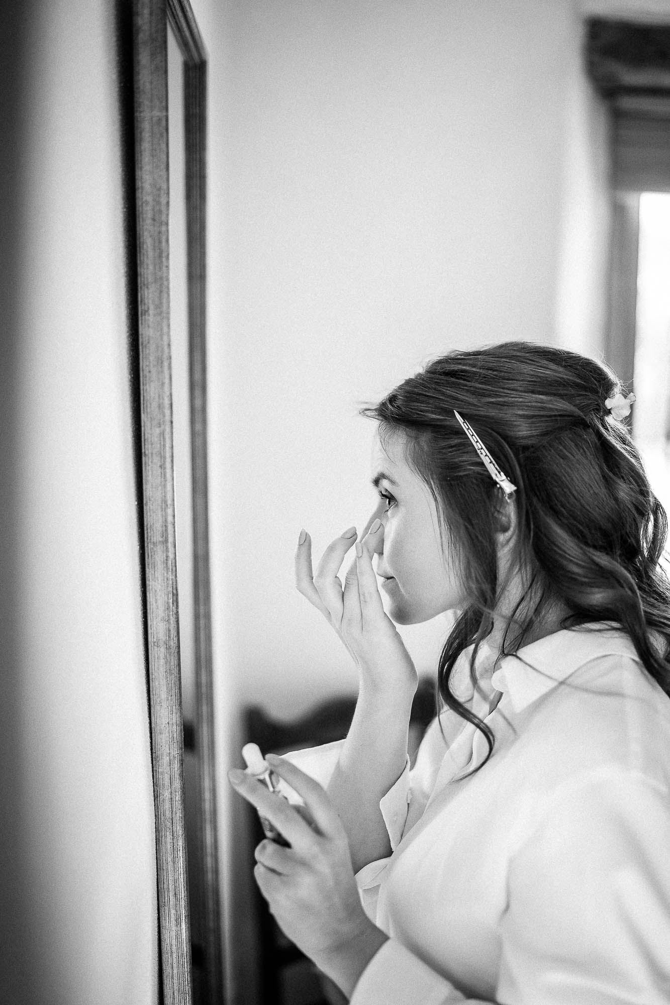 Bride applying makeup in mirror during wedding morning preparations