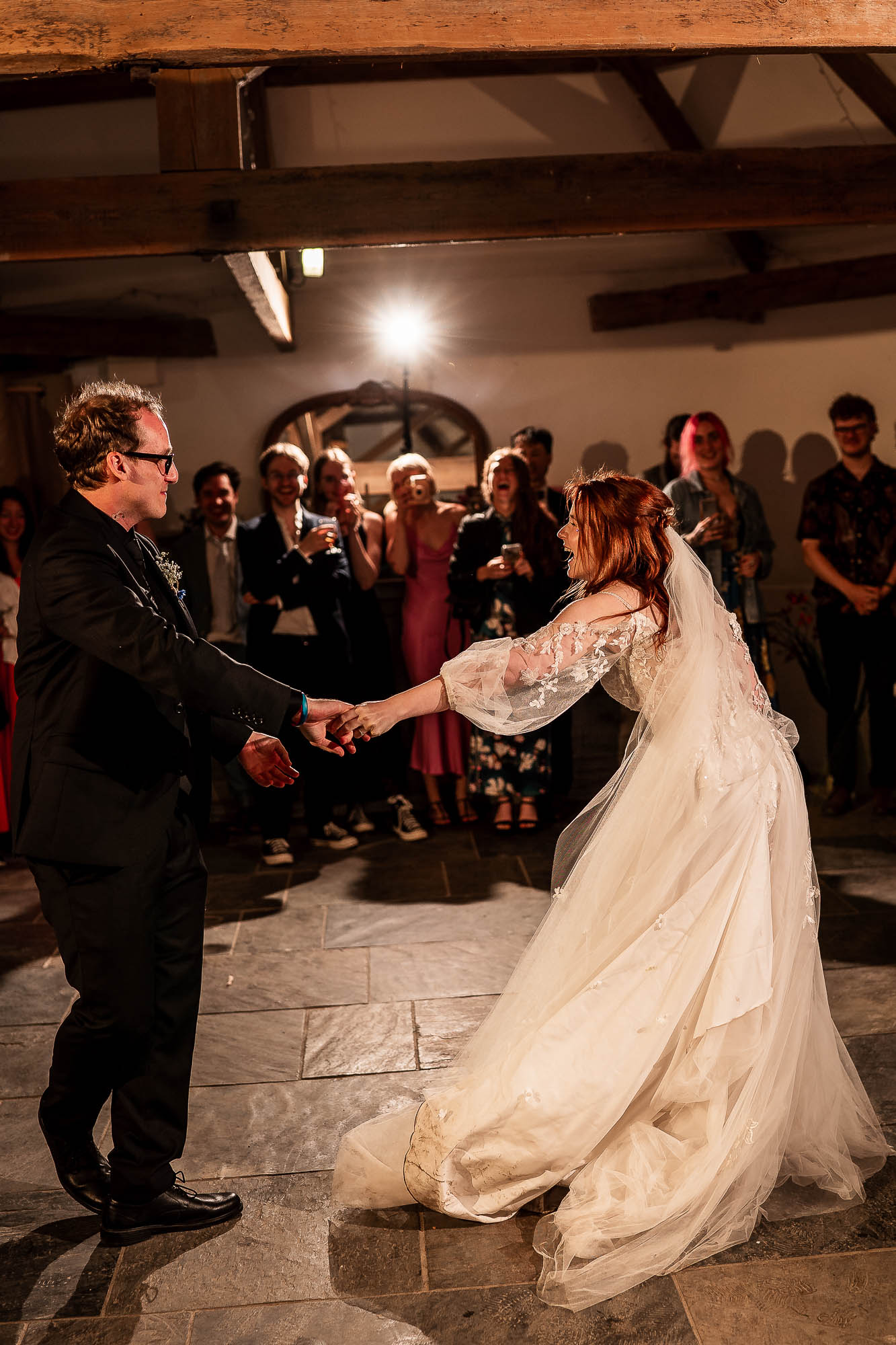 Bride and groom laughing while holding hands on rustic barn dance floor in Devon