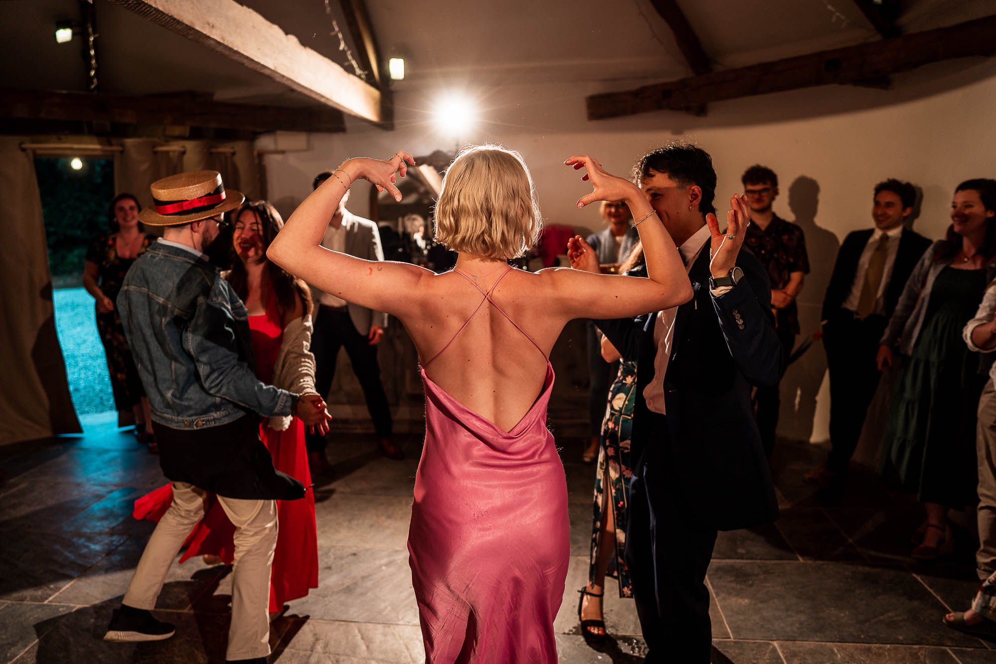 Guest in pink dress dancing with arms raised at lively wedding party