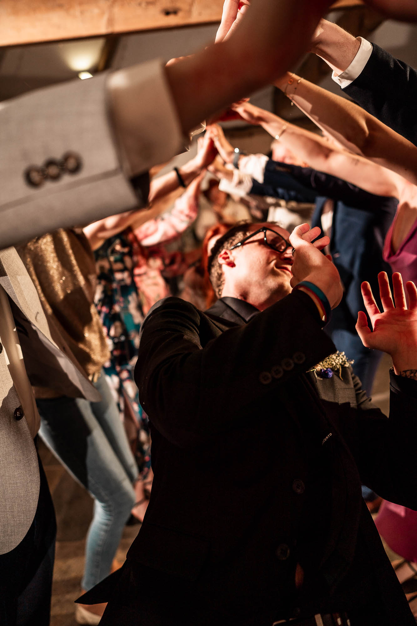 Groom dancing beneath tunnel of guests at lively barn wedding reception