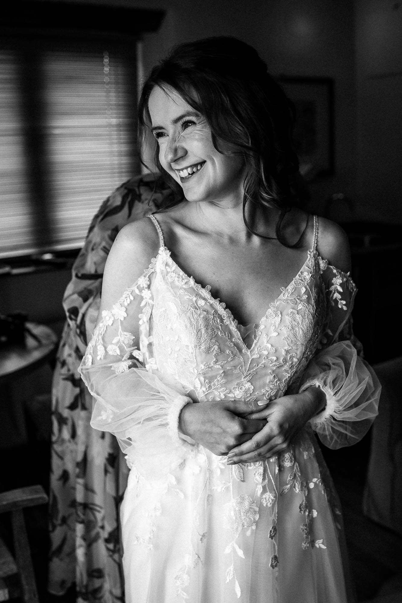 Bride smiling by window light in embroidered lace wedding dress during bridal preparations at Wonwood Barton