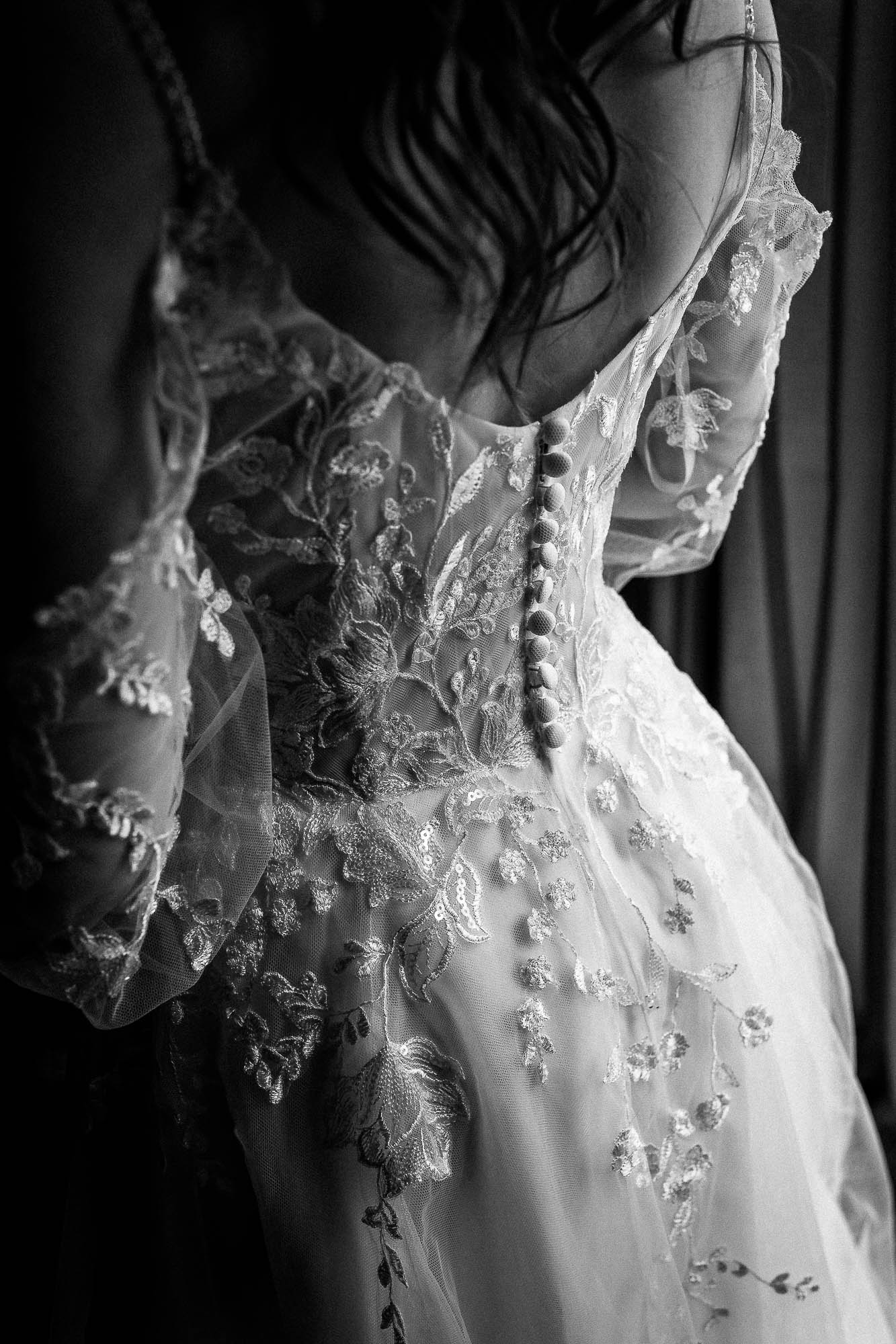 Detail of lace wedding dress buttons and embroidered sleeves in soft window light at Wonwood Barton