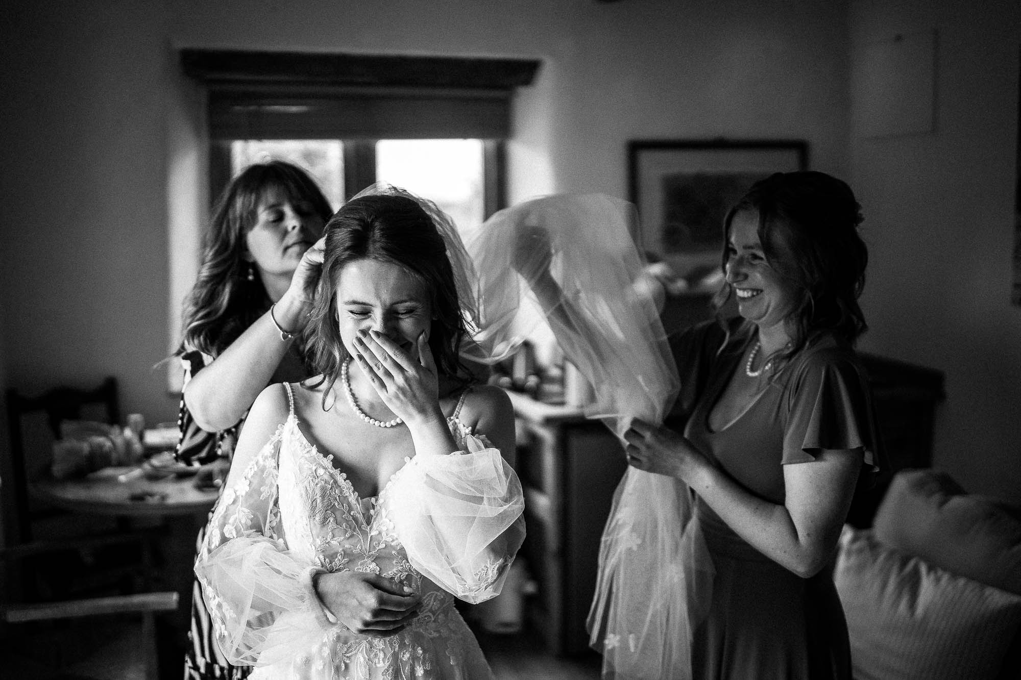 Bridesmaids helping bride with veil during candid getting ready moments at Wonwood Barton