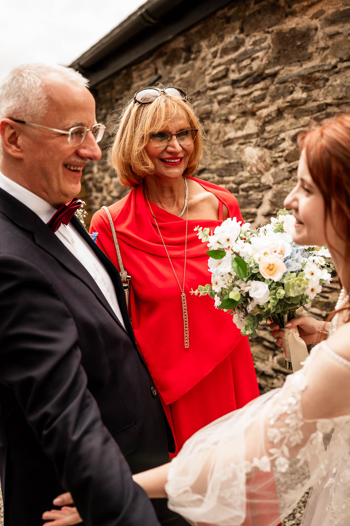 Bride chatting with parents beside stone wall at Wonwood Barton wedding reception