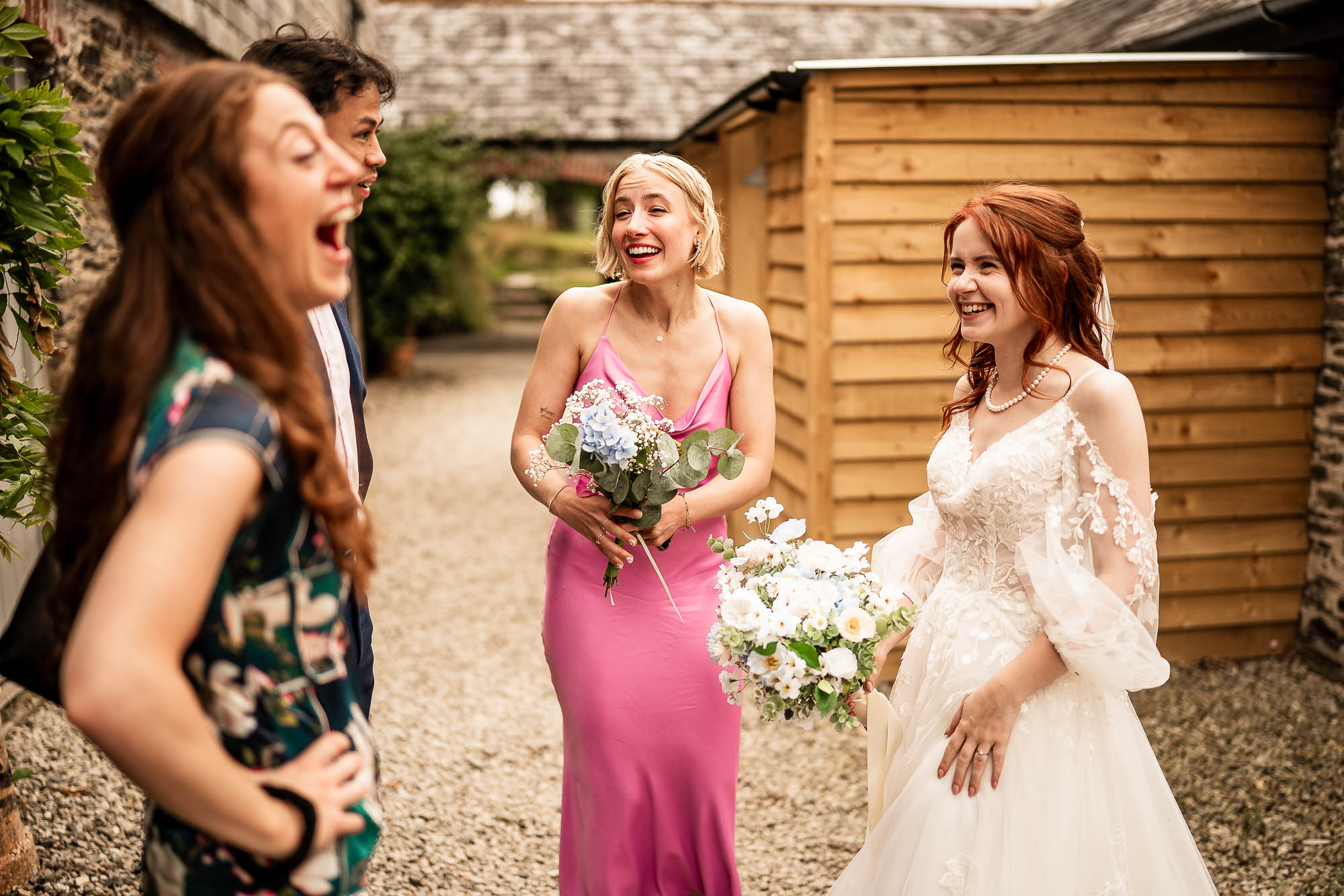 Bride laughing with bridesmaids in courtyard at Wonwood Barton wedding in Devon
