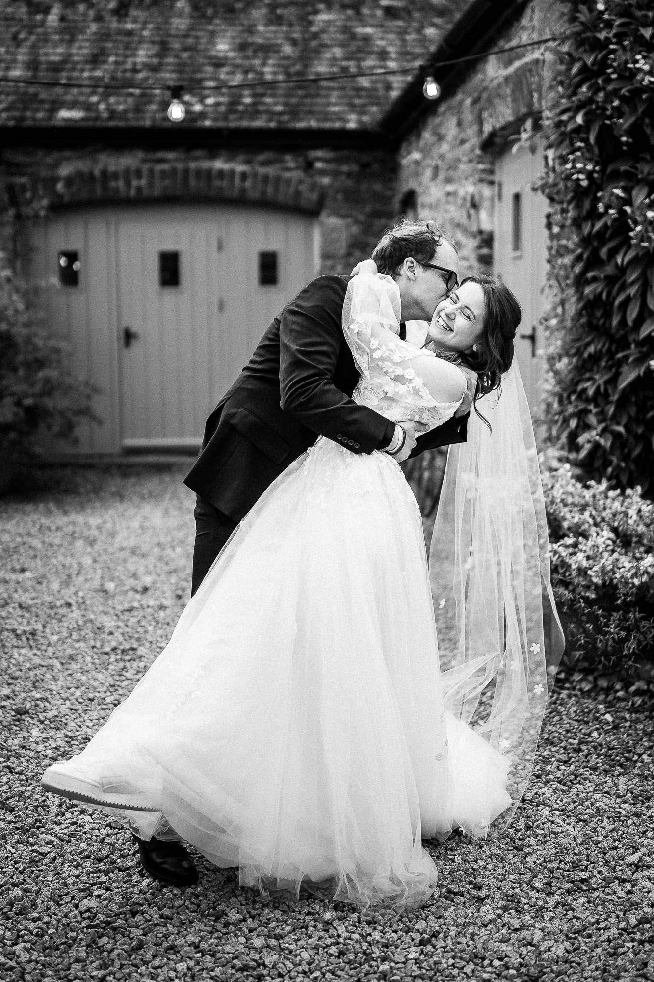 Groom kissing bride during romantic dip in courtyard at Wonwood Barton wedding