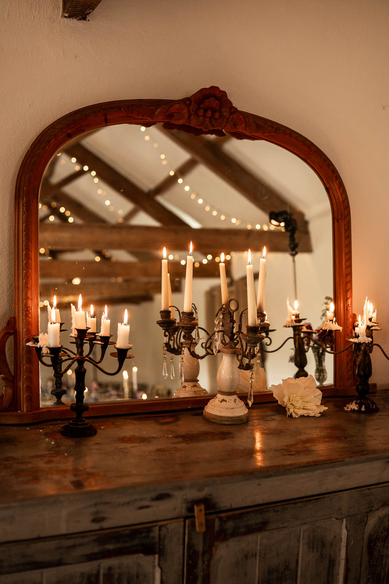 Lit candelabras reflected in vintage mirror inside Wonwood Barton barn wedding reception